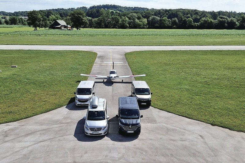 Four TourSlo minibuses and a light aircraft on an airfield taxiway, drone view