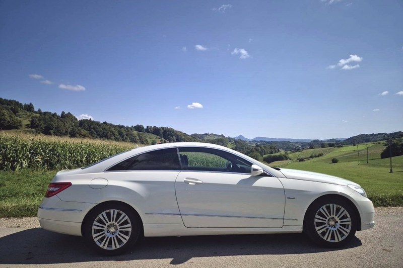 White Mercedes E-Class coupé of TourSlo, side view among hills